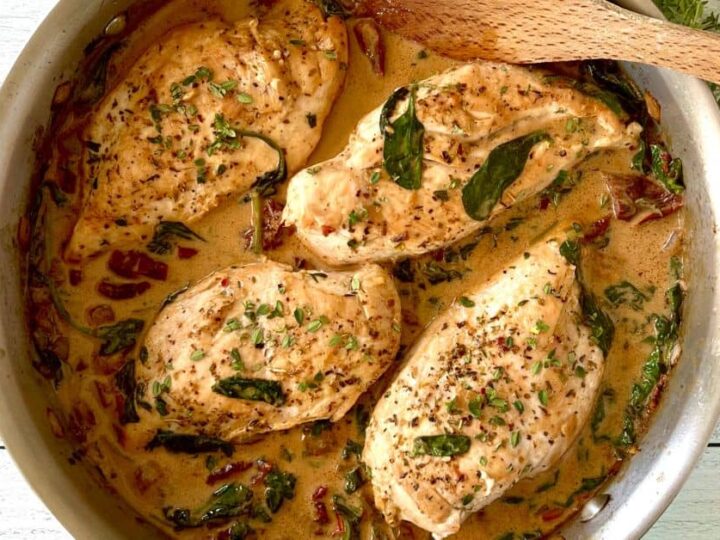 Chicken breasts in a pan with a wooden spoon.