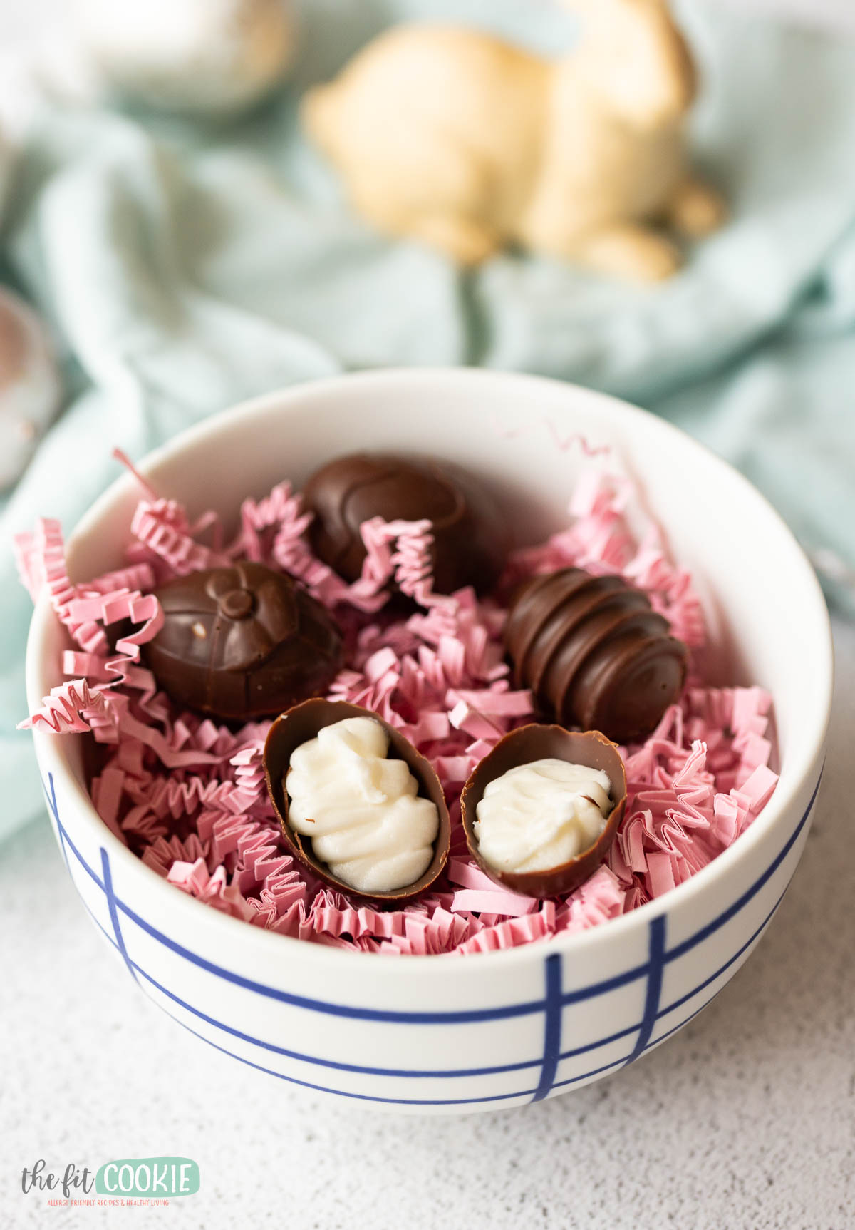 A bowl of chocolate cream eggs and confections with some pieces decoratively cut to show filling, presented on a bed of pink crinkle paper.