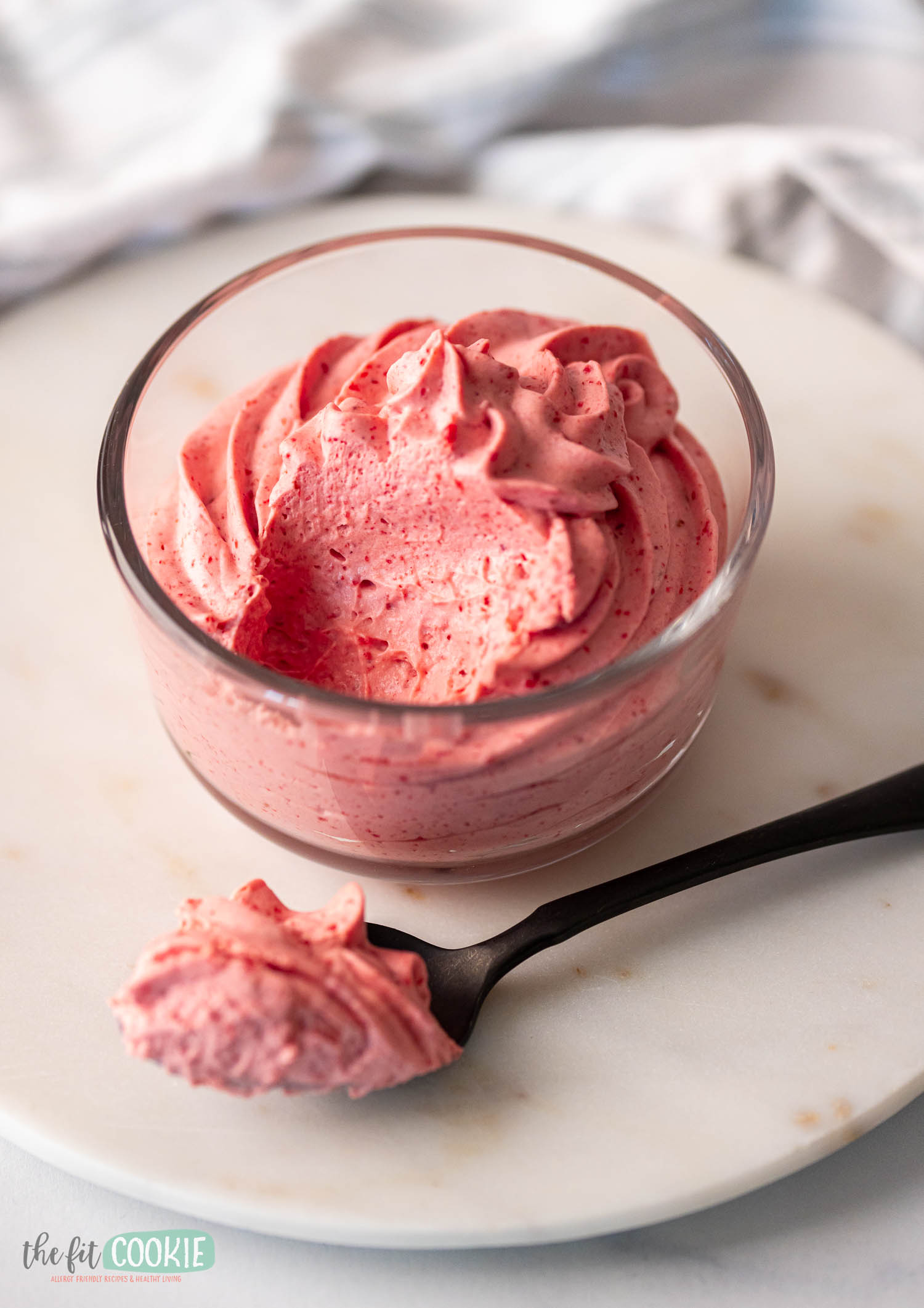 A bowl of creamy strawberry mousse in a glass dish with a black spoon.