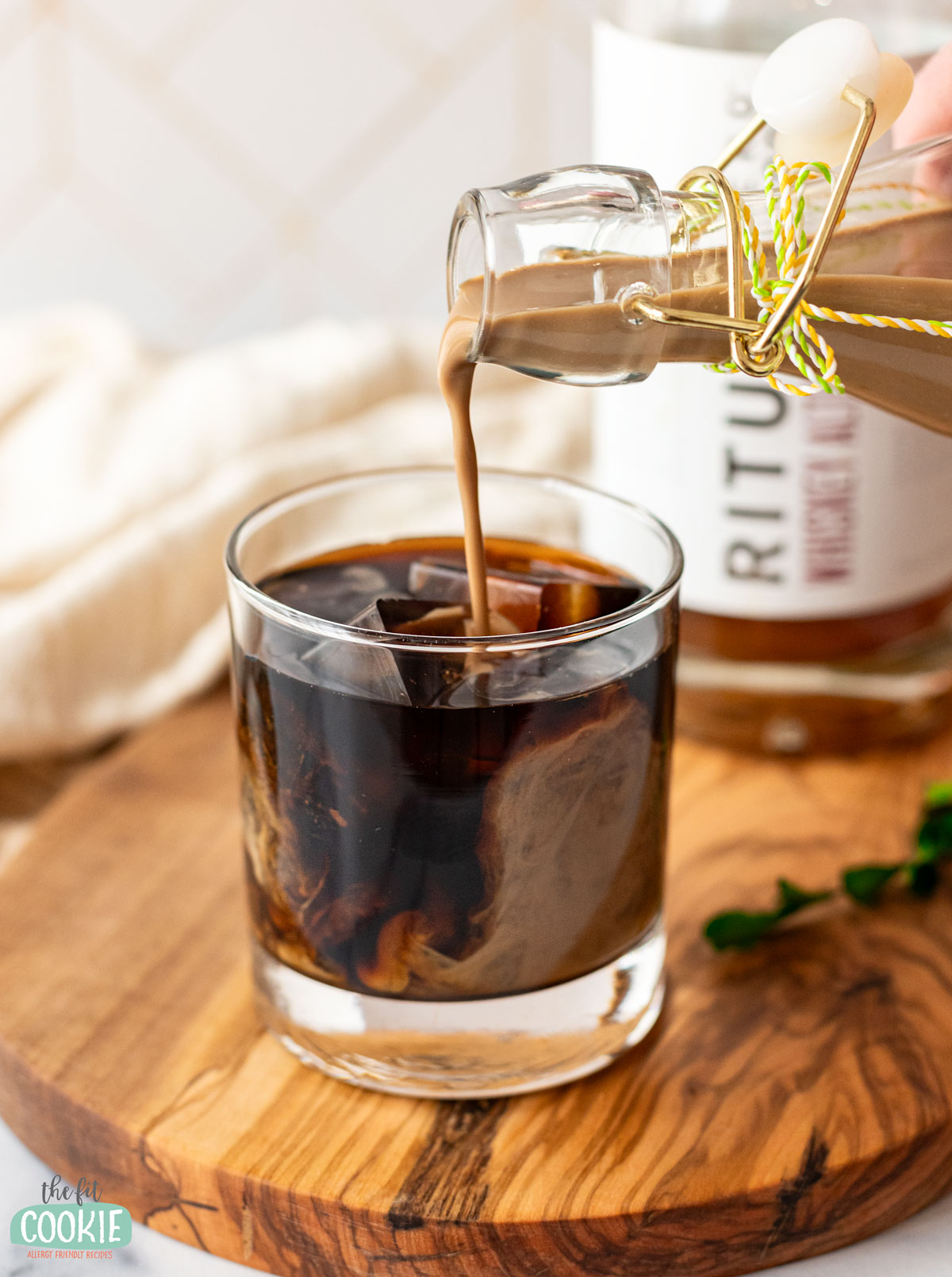 A person pouring dairy-free Baileys into a glass of iced coffee.