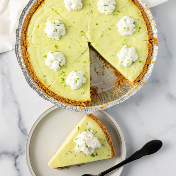 A key lime pie with a single slice served on a plate, topped with whipped cream and lime zest.