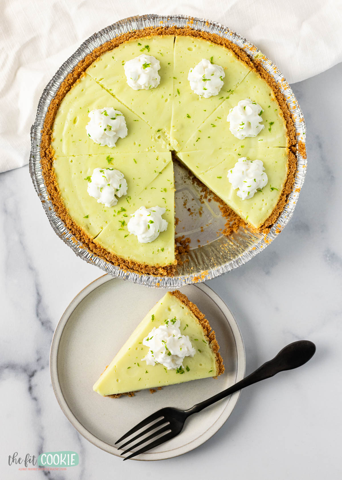 A key lime pie with a single slice served on a plate, topped with whipped cream and lime zest.