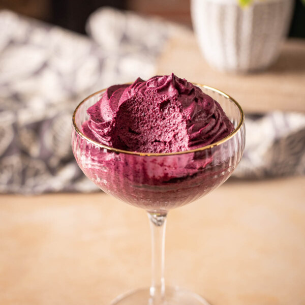 A scooped serving of purple acai berry sorbet in a glass dessert bowl.