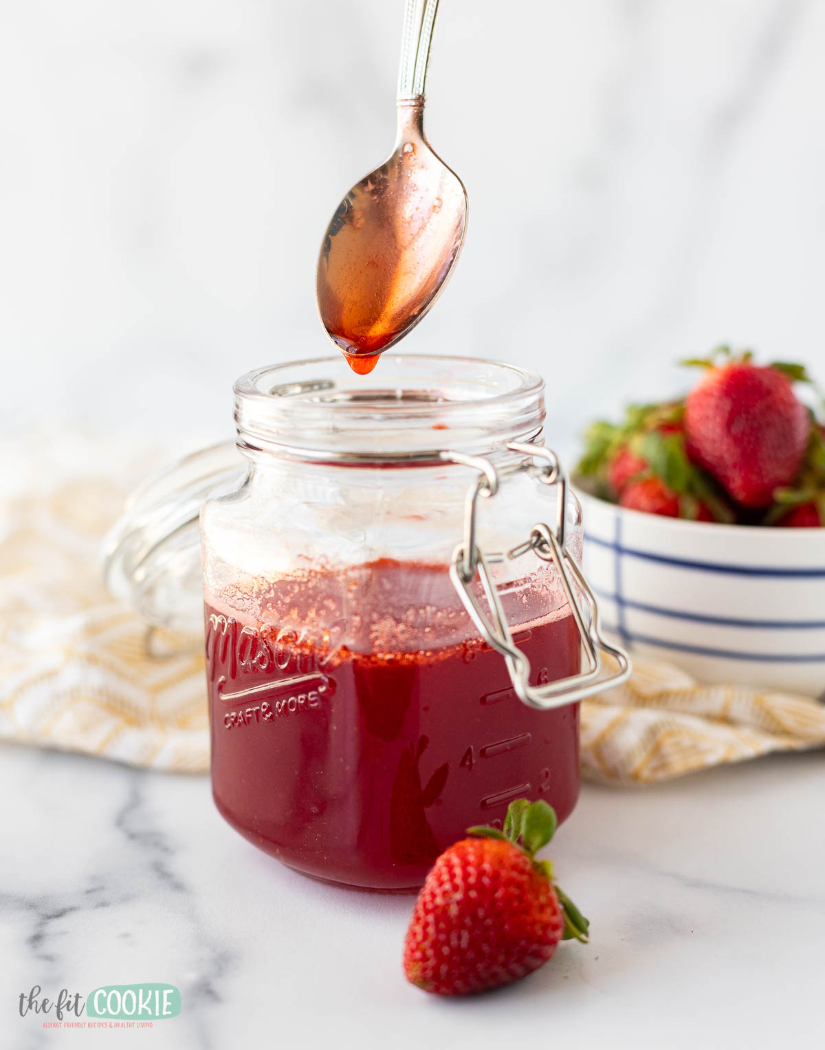 A jar of homemade strawberry simple syrup with a spoon dripping syrup into it.