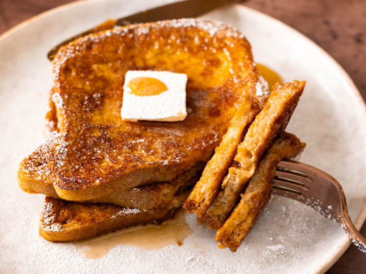French toast, infused with delightful pumpkin spice, topped with butter and syrup on a plate, with a forkful cut and lifted.
