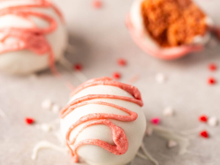 A close-up of a white chocolate-covered Oreo truffle with pink drizzle, surrounded by small heart-shaped sprinkles, offers a delightful Berry Pink touch. Perfectly crafted to be gluten-free, this treat embodies both elegance and indulgence in every bite.