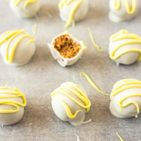 Gluten free lemon Oreo truffles coated in white chocolate with yellow drizzle are arranged on parchment paper; one truffle is cut open to show a crumbly interior.