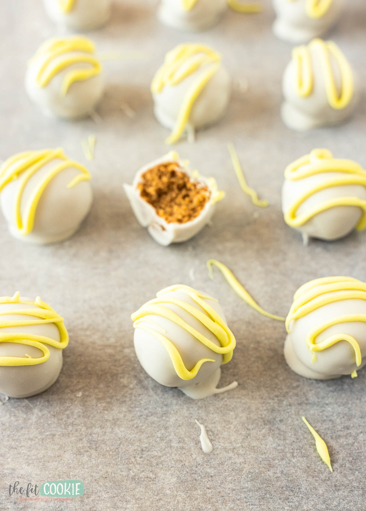 Gluten free lemon Oreo truffles coated in white chocolate with yellow drizzle are arranged on parchment paper; one truffle is cut open to show a crumbly interior.