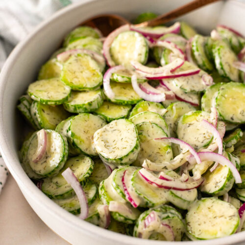 A bowl of Dairy Free cucumber salad with sliced cucumbers, red onions, and a creamy dill dressing, served with a spoon.