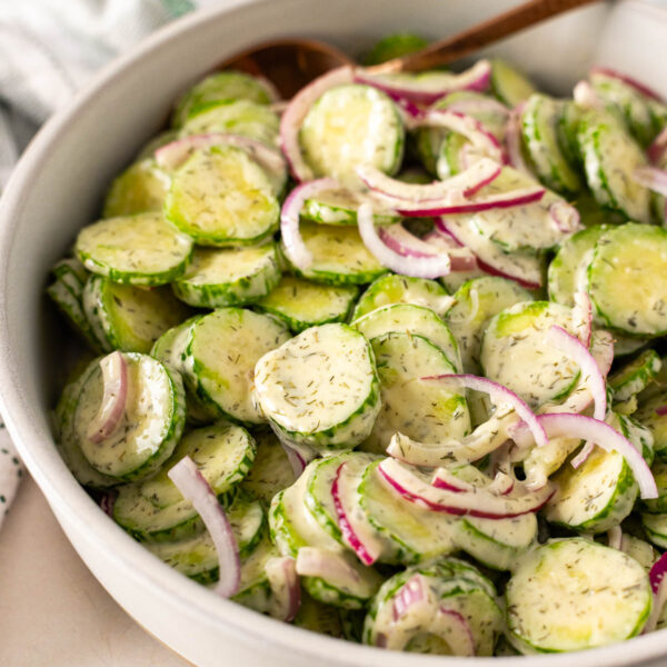 A bowl of Dairy Free cucumber salad with sliced cucumbers, red onions, and a creamy dill dressing, served with a spoon.