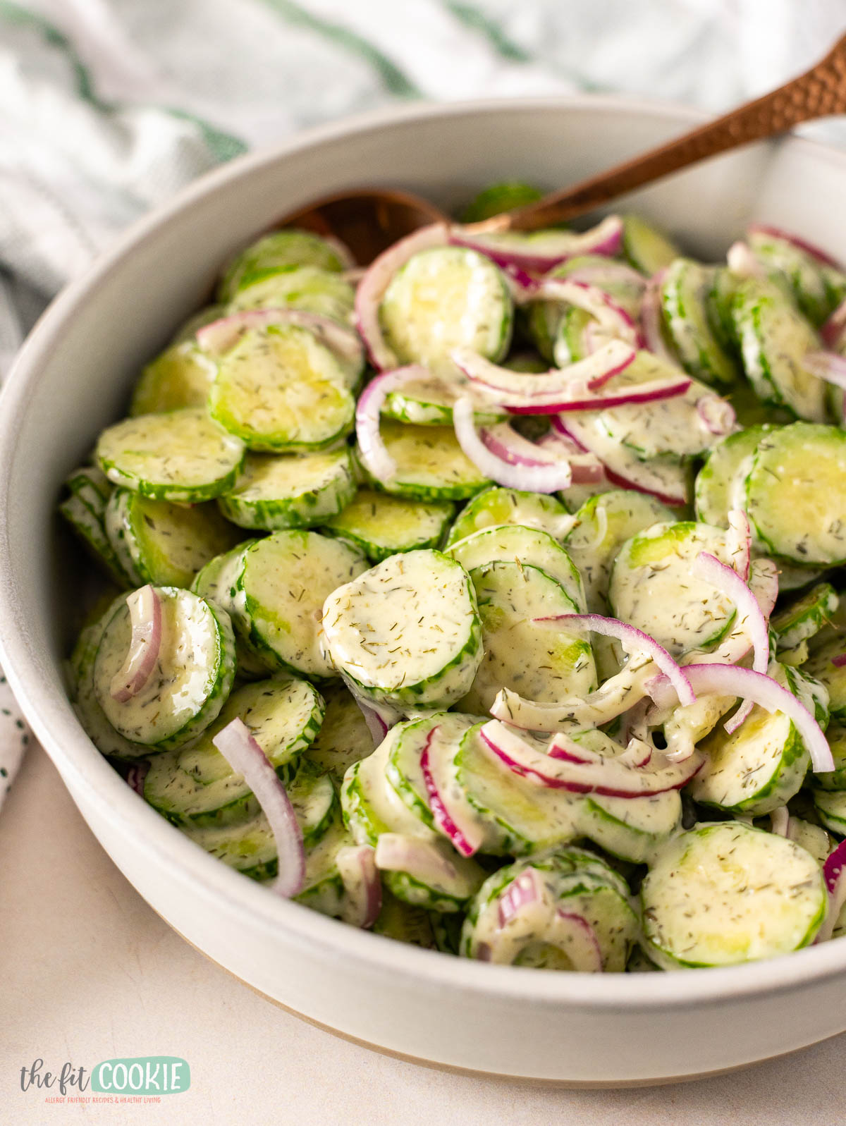A bowl of Dairy Free cucumber salad with sliced cucumbers, red onions, and a creamy dill dressing, served with a spoon.