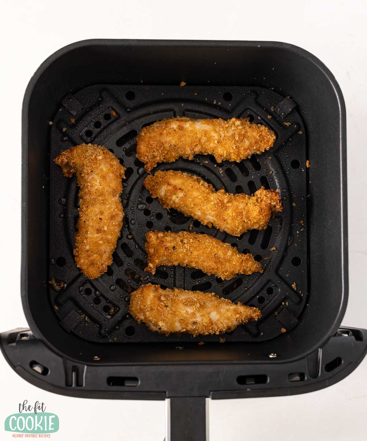 Five gluten free air fryer chicken tenders are arranged in the basket of an air fryer, after being air fried.