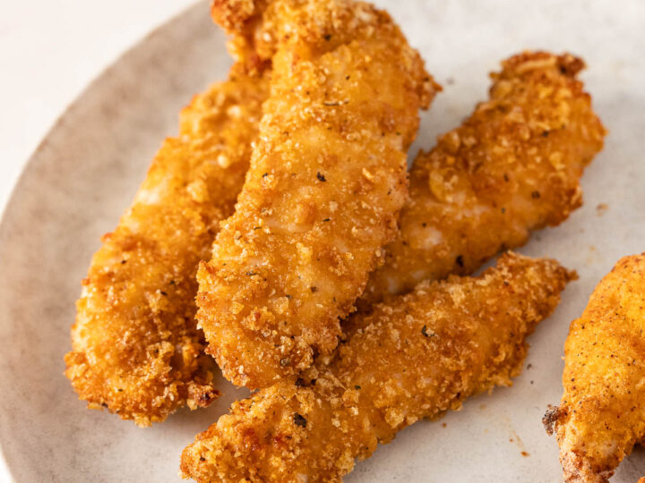 Four gluten free air fryer chicken tenders arranged on a white plate.