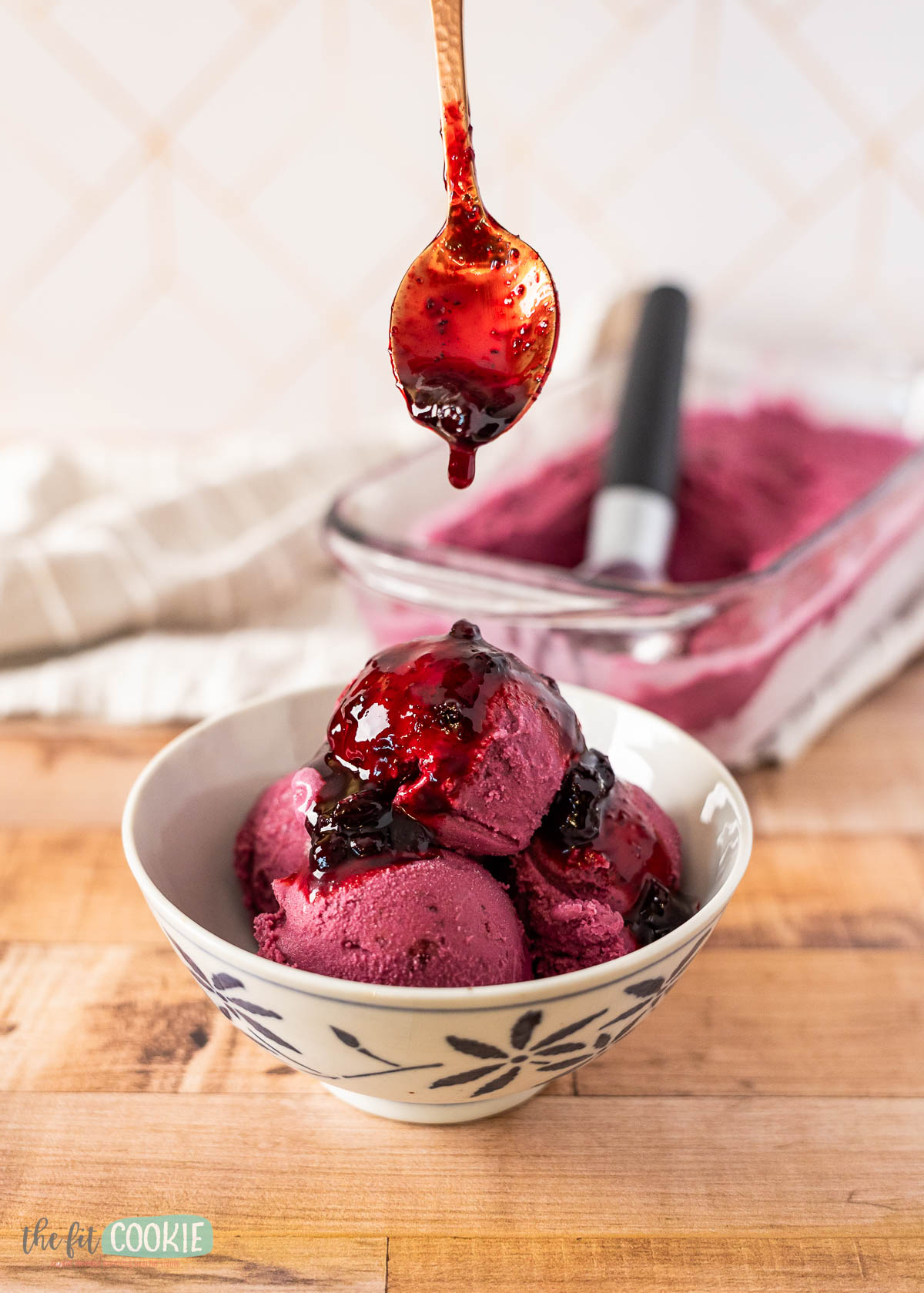 A bowl of dairy free huckleberry ice cream is topped with homemade huckleberry sauce, with a spoon holding more sauce above it. 