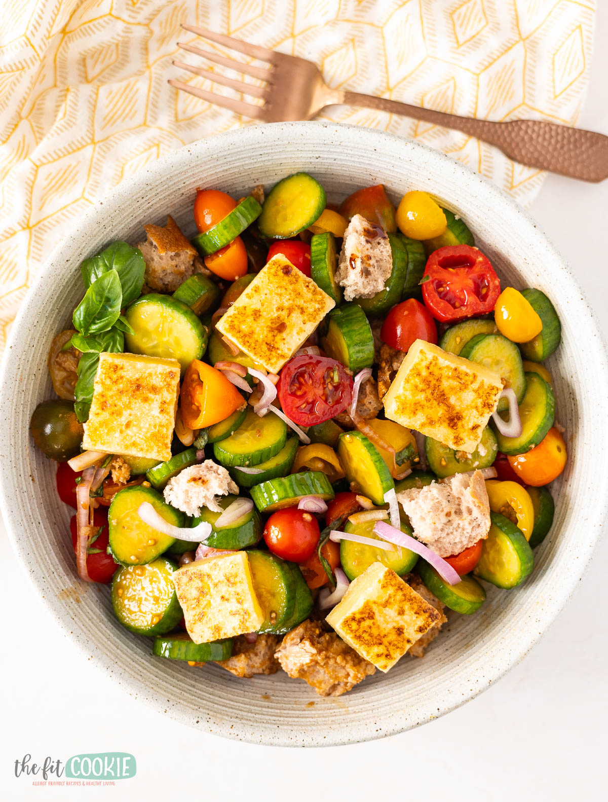 A colorful panzanella salad in a white speckled boal next to a copper fork.