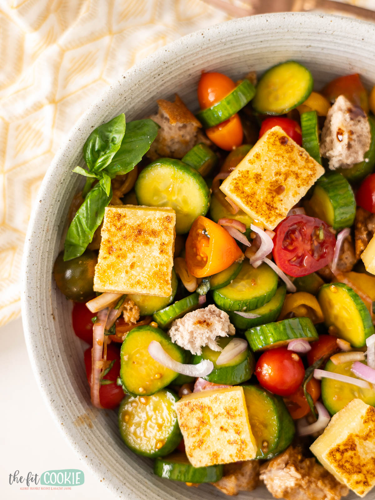 A bowl of gluten free balsamic panzanella salad with sliced cucumbers, cherry tomatoes, and fresh basil.