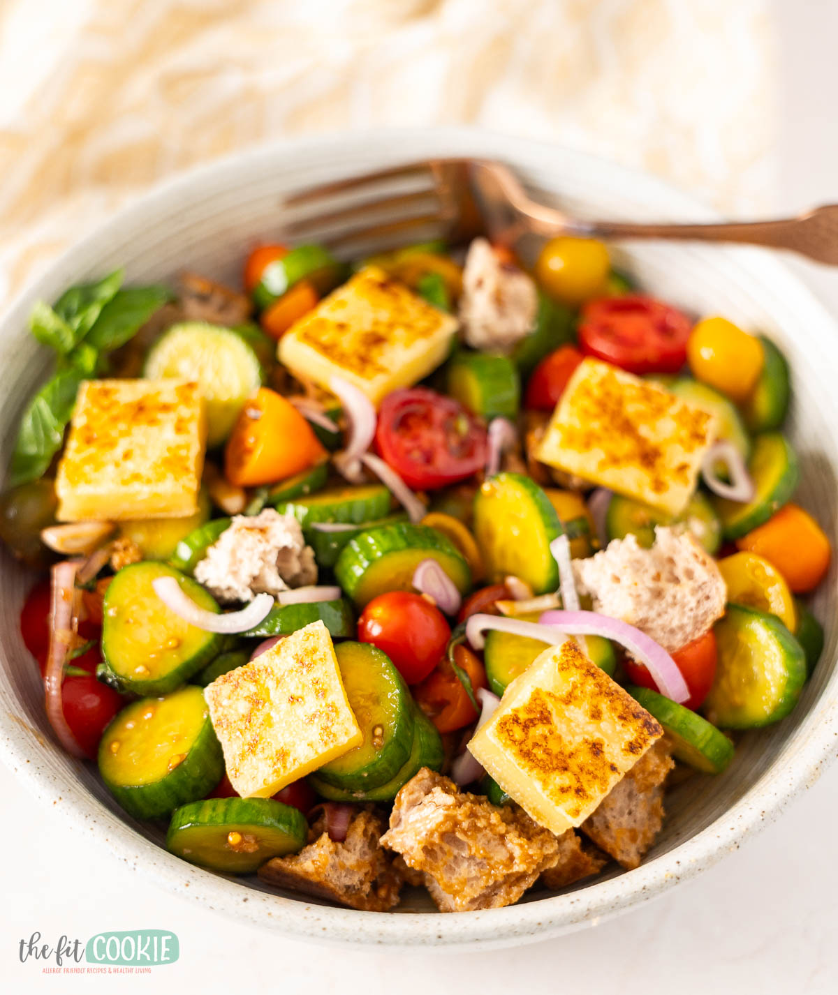 A vibrant panzanella salad featuring grilled dairy free halloumi, and gluten free bread.