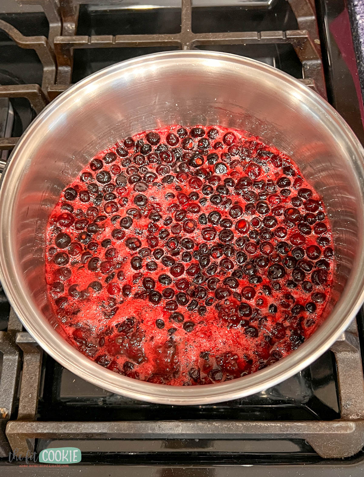 A stainless steel pot of simmering huckleberries sits on a gas stove.