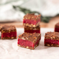 Four Dairy Free Bing Bars with a chocolate coating, vibrant red layer, and nutty base are displayed on parchment paper, set against a softly blurred background.