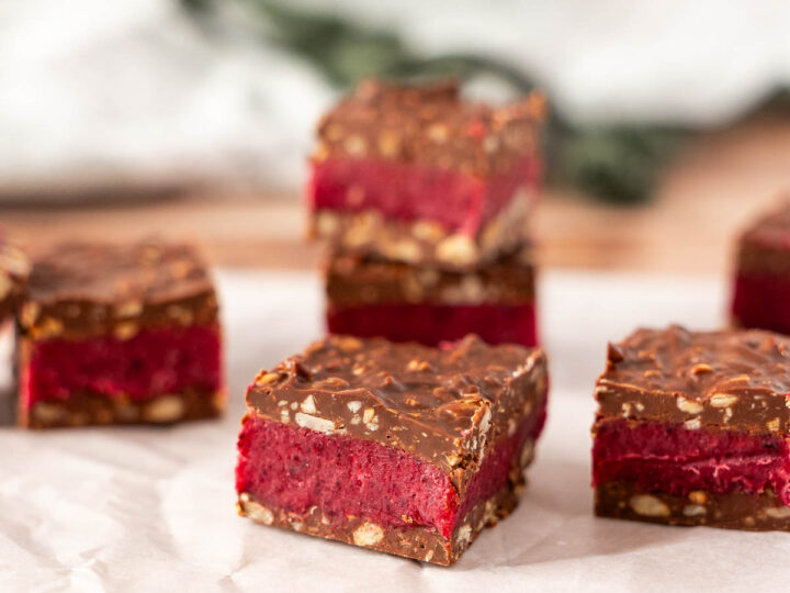 Four Dairy Free Bing Bars with a chocolate coating, vibrant red layer, and nutty base are displayed on parchment paper, set against a softly blurred background.