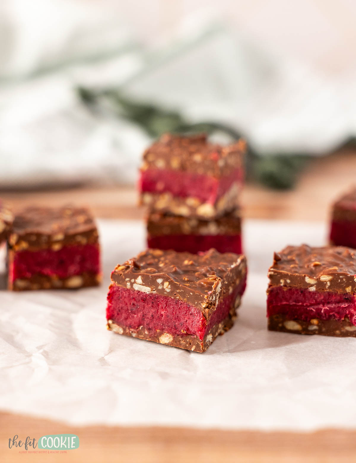 Four Dairy Free Bing Bars with a chocolate coating, vibrant red layer, and nutty base are displayed on parchment paper, set against a softly blurred background.
