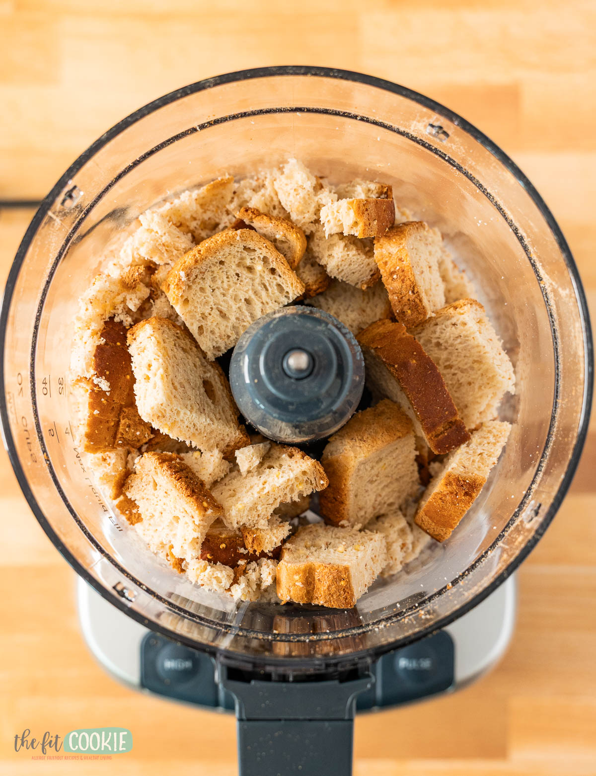 Cubed pieces of bread inside a food processor on a wooden surface, ready to be processed into gluten free seasoned bread crumbs.