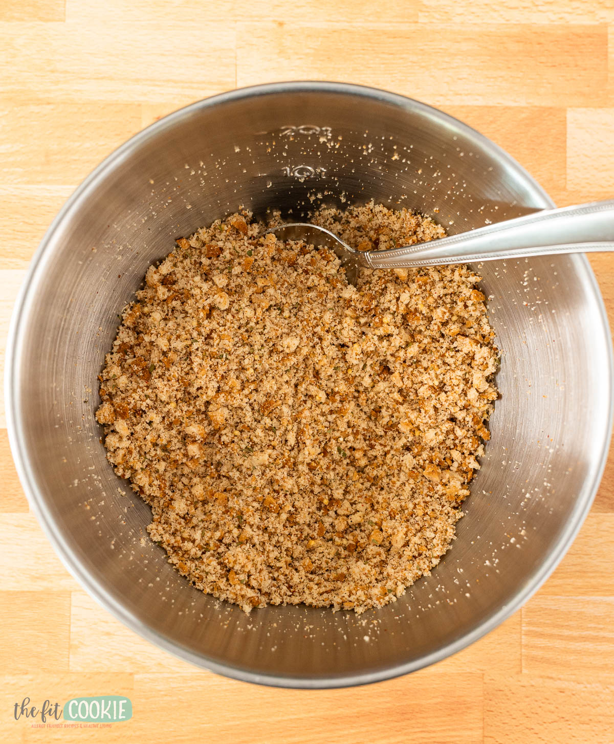 A metal mixing bowl containing gluten free bread crumbs mixed with seasonings.