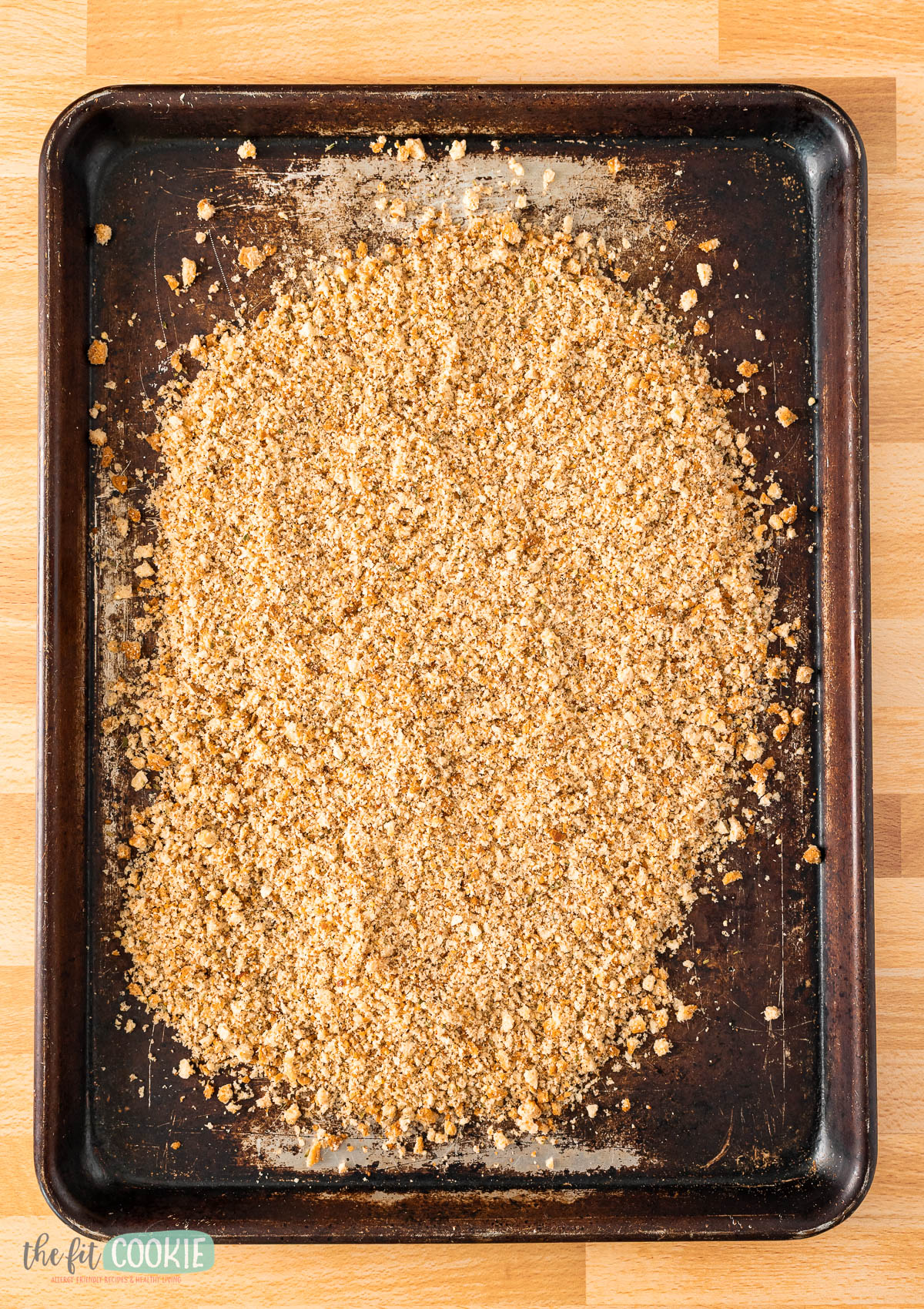 A baking sheet covered with an even layer of unbaked gluten free seasoned bread crumbs.