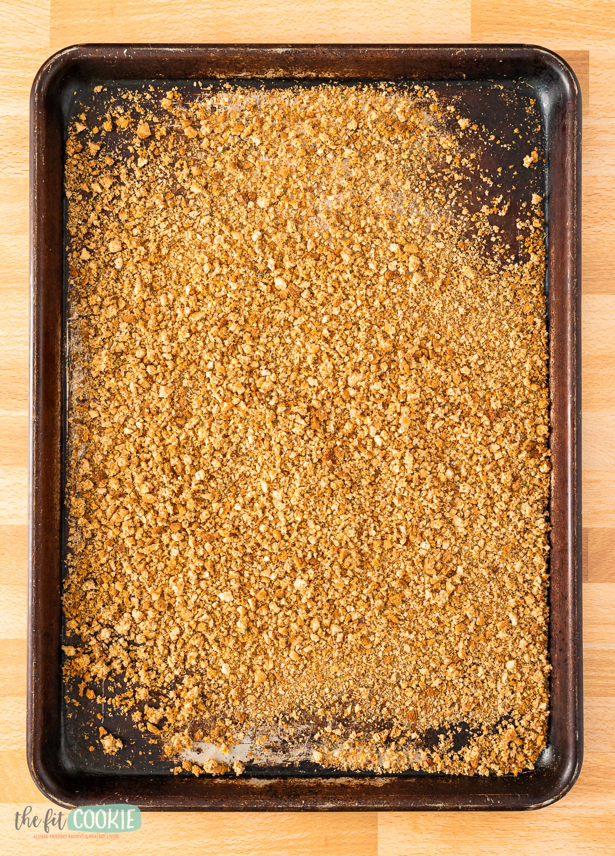 A baking sheet filled with an even layer of golden brown toasted oat, nut mixture, and gluten free seasoned bread crumbs on a wooden surface.
