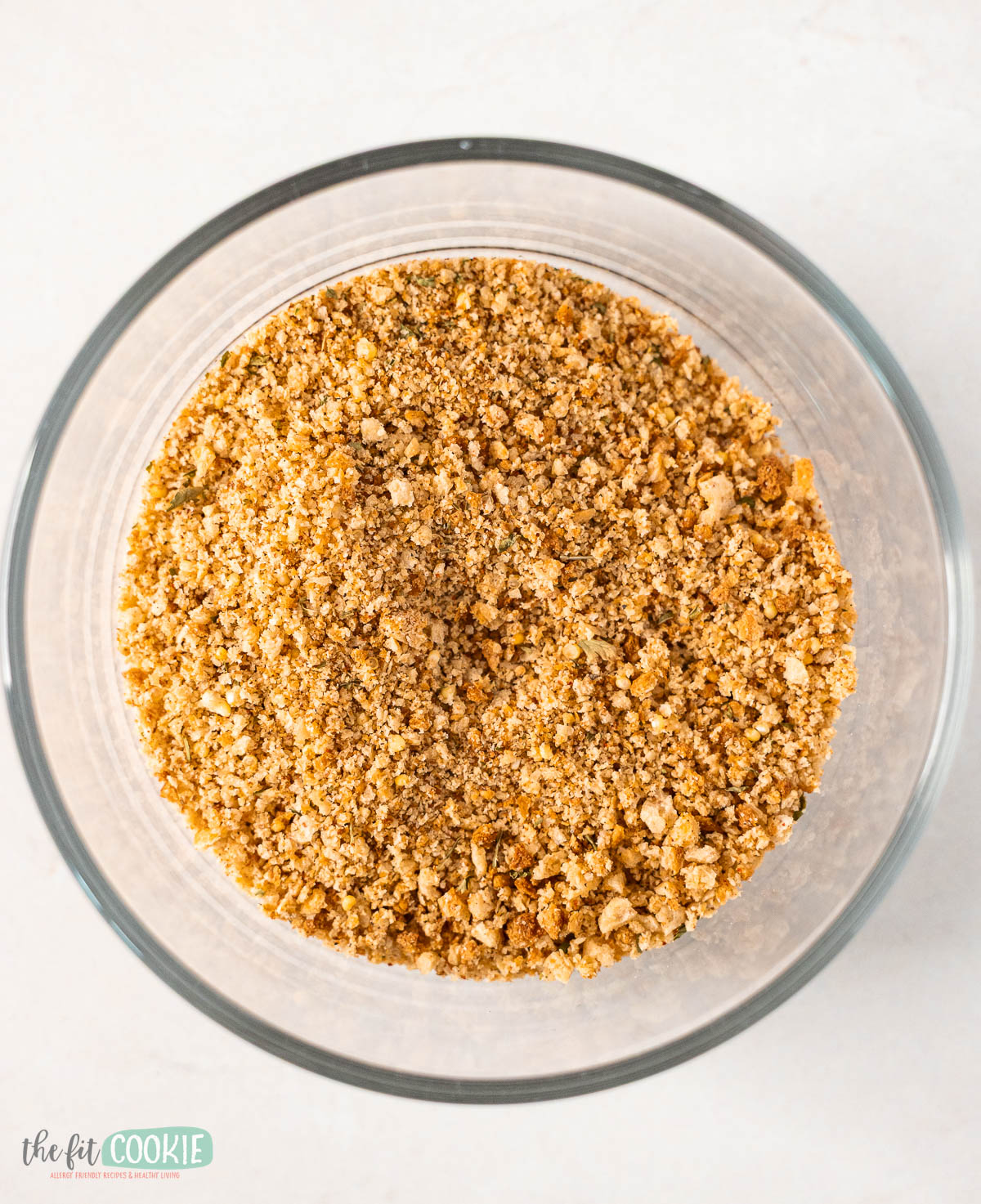 A clear glass bowl filled with finely ground, golden-brown Gluten Free Bread Crumbs sits on a white surface, ready to add crunch and flavor to your favorite recipes.