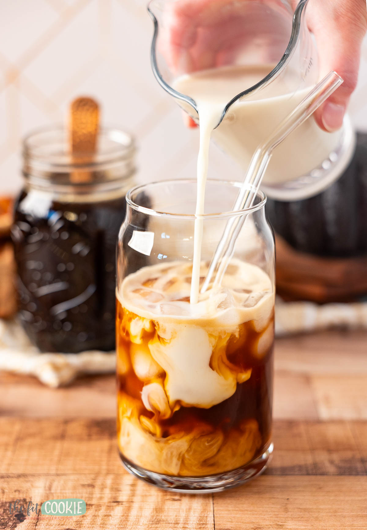glass of iced coffee with oatmilk being poured in.