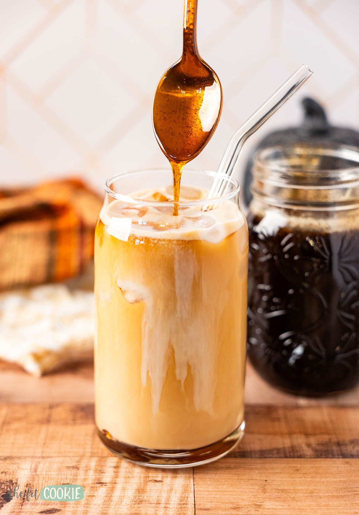 A glass of iced oatmilk coffee with pumpkin brown sugar syrup being drizzled in.