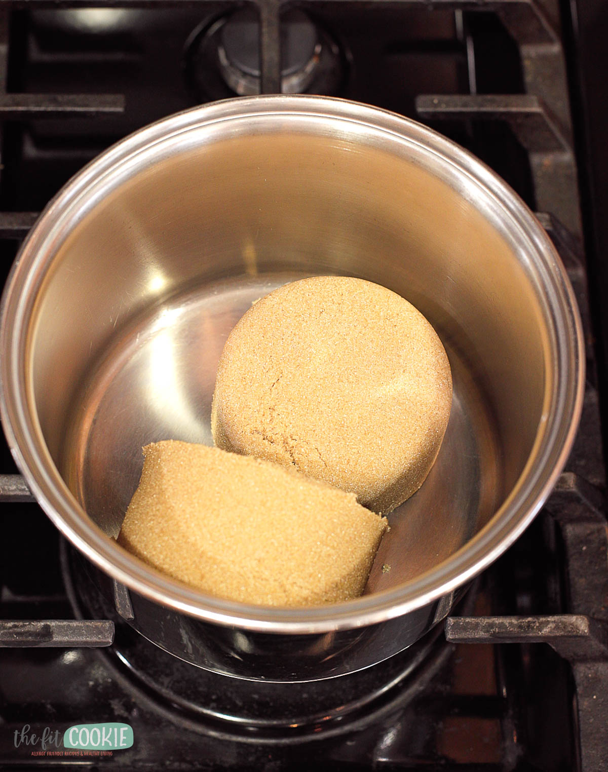 Two cups of brown sugar in a stainless steel saucepan on a stove burner.