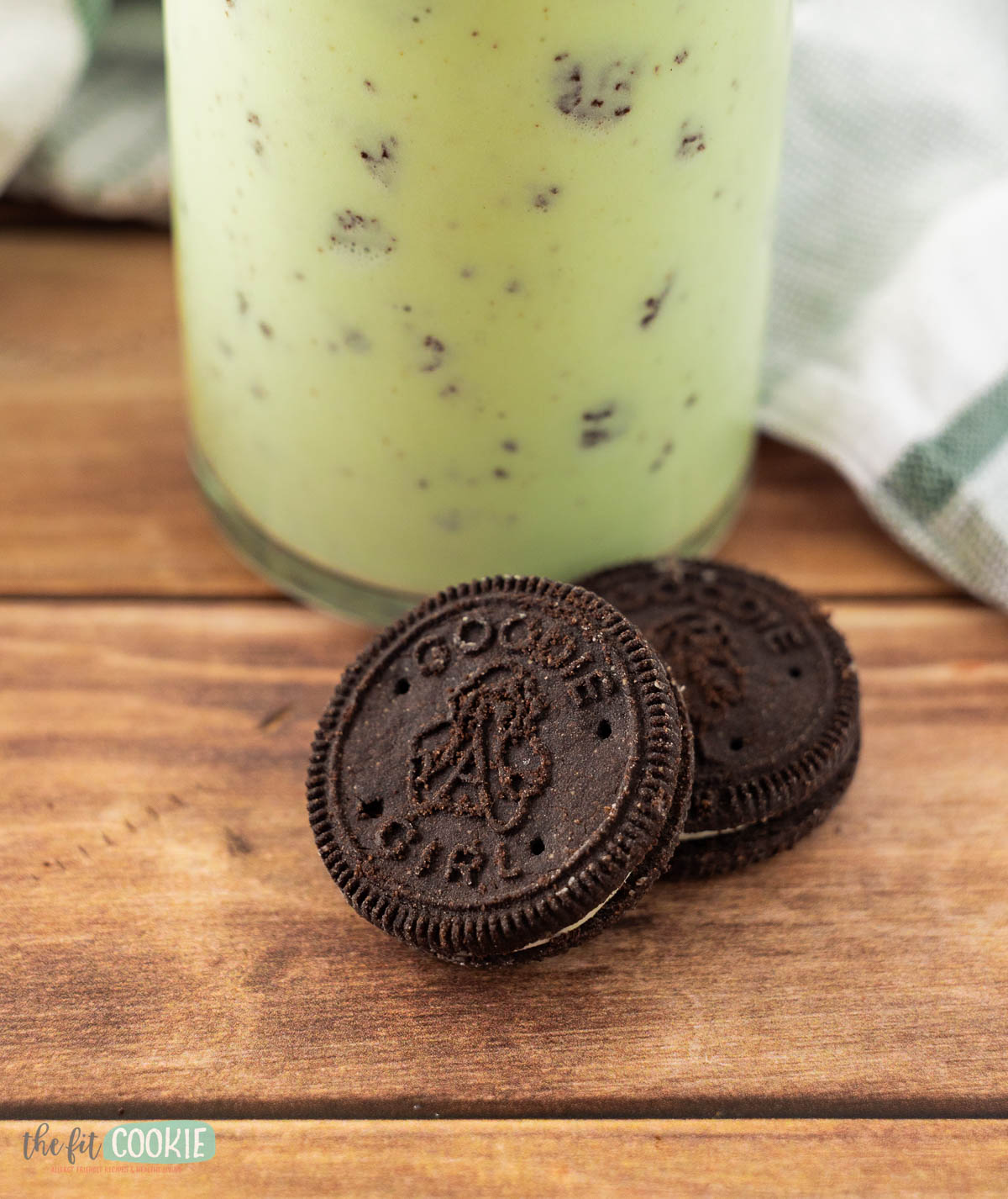 2 goodie girl chocolate sandwich cookies in front of a glass of dairy free shamrock shake.