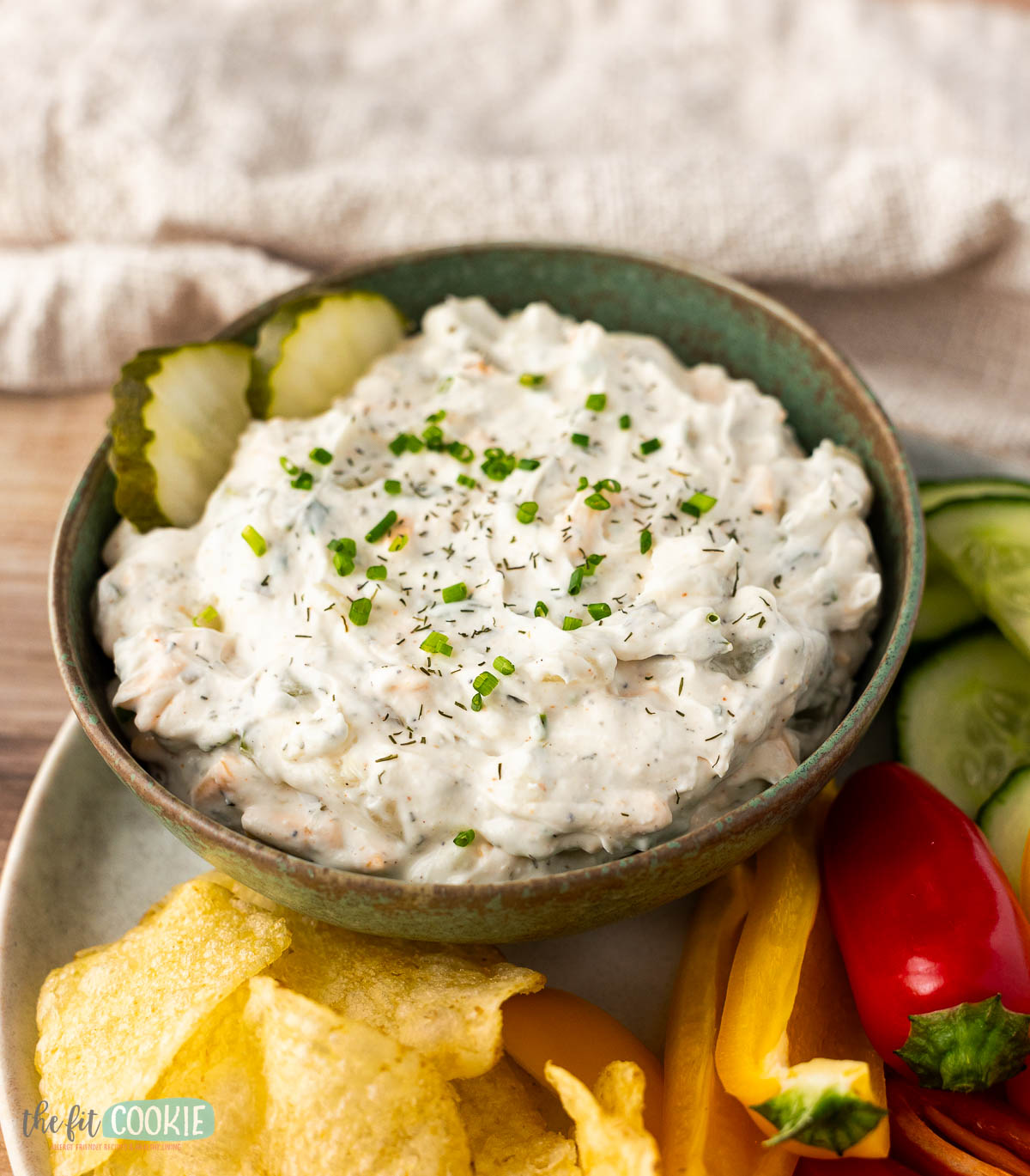 A green bowl of dairy free dill pickle dip topped with chopped chives and dill.