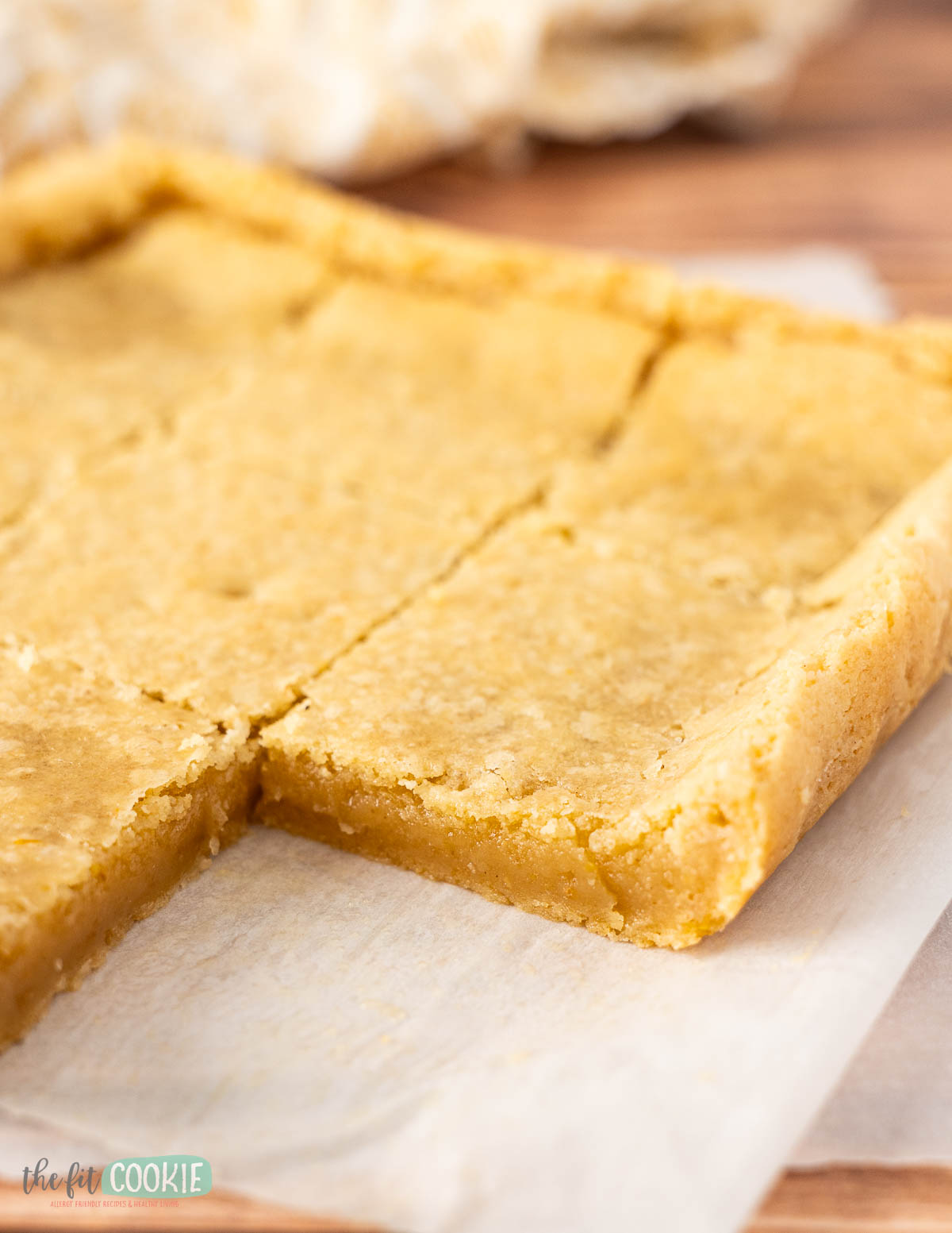A close-up of a partially sliced pan of vegan lemon cookie bars on parchment paper.