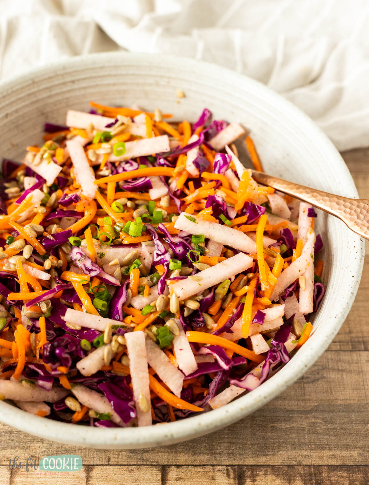 A colorful crunchy jicama salad in a white bowl with a copper spoon.