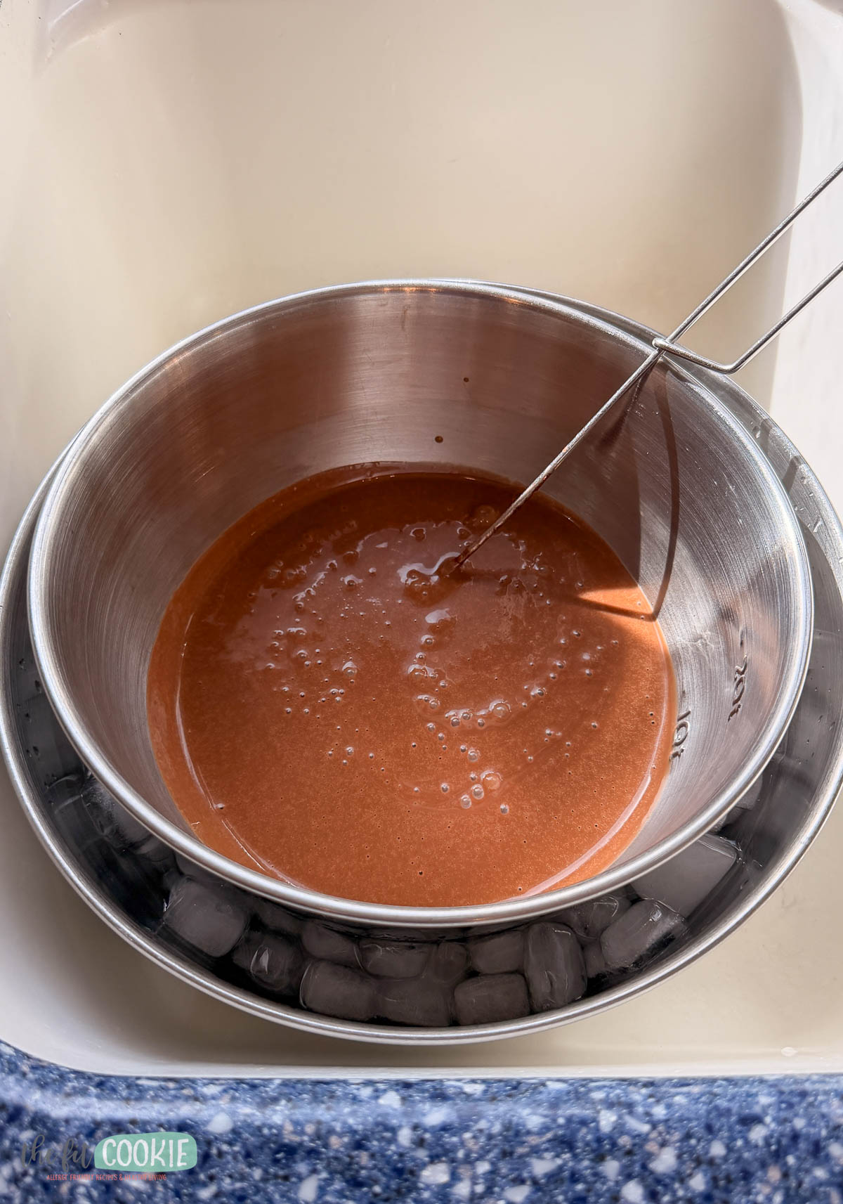 A metal bowl with dairy free chocolate ice cream mixture and a whisk sits in a larger bowl filled with ice cubes.