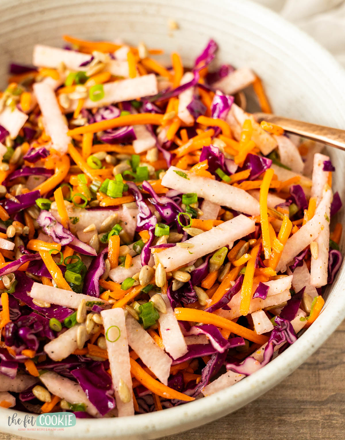 A bowl of jicama salad with shredded red cabbage, carrots, green onions, and sunflower seeds, all mixed together.
