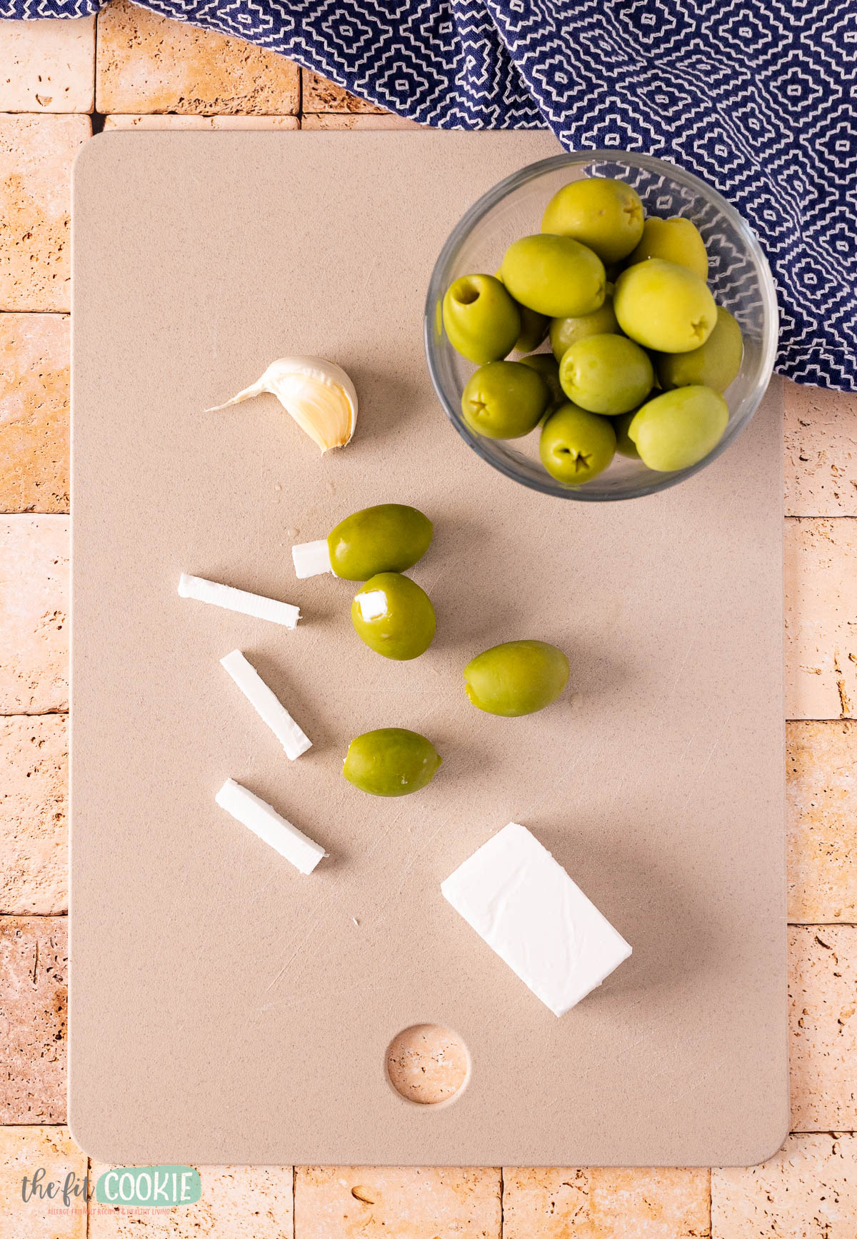 A cutting board with olives and dairy free feta cheese cut into pieces.