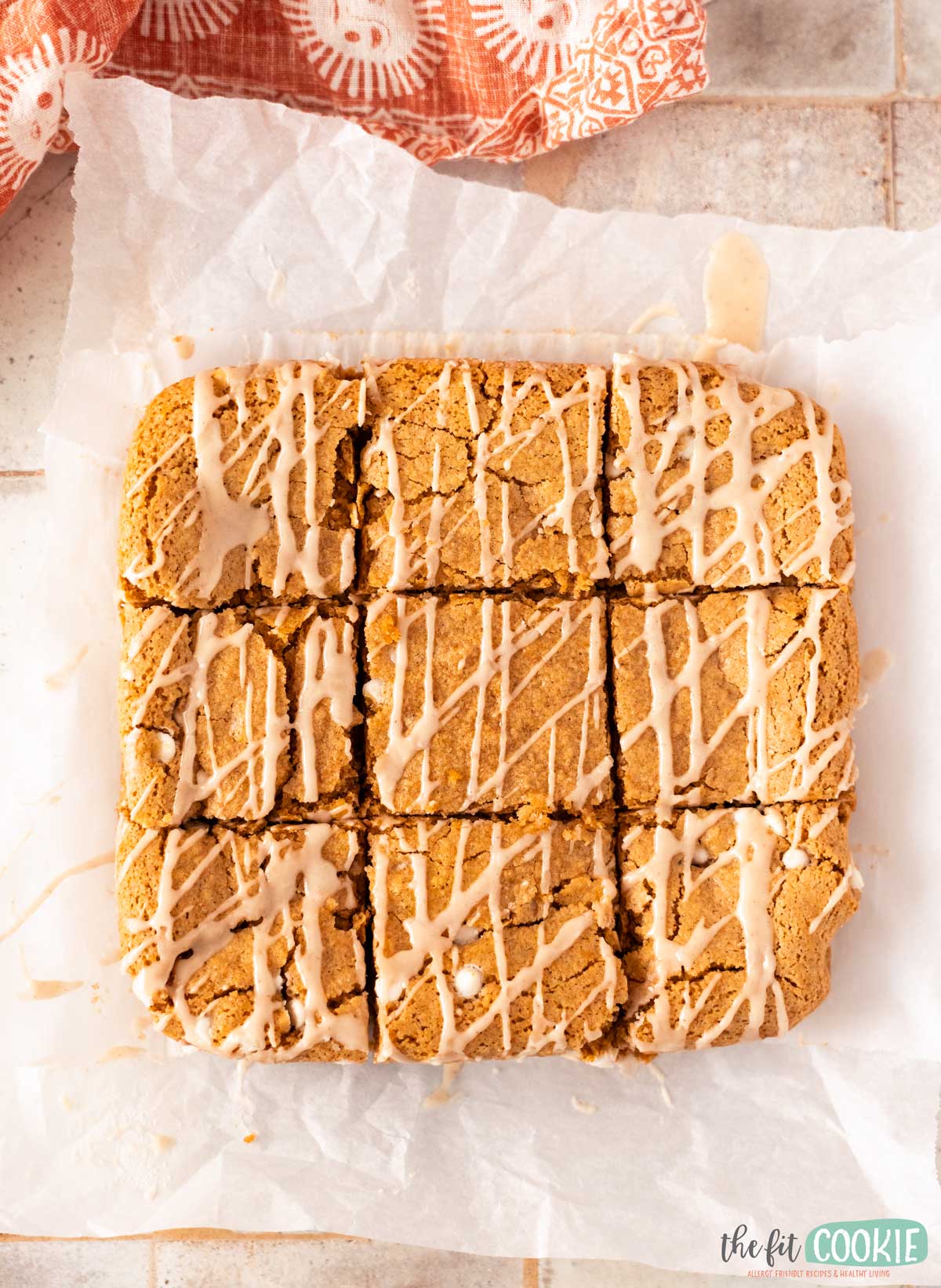 A square slab of sliced cinnamon roll blondies cut into nine pieces, topped with a drizzle of icing.