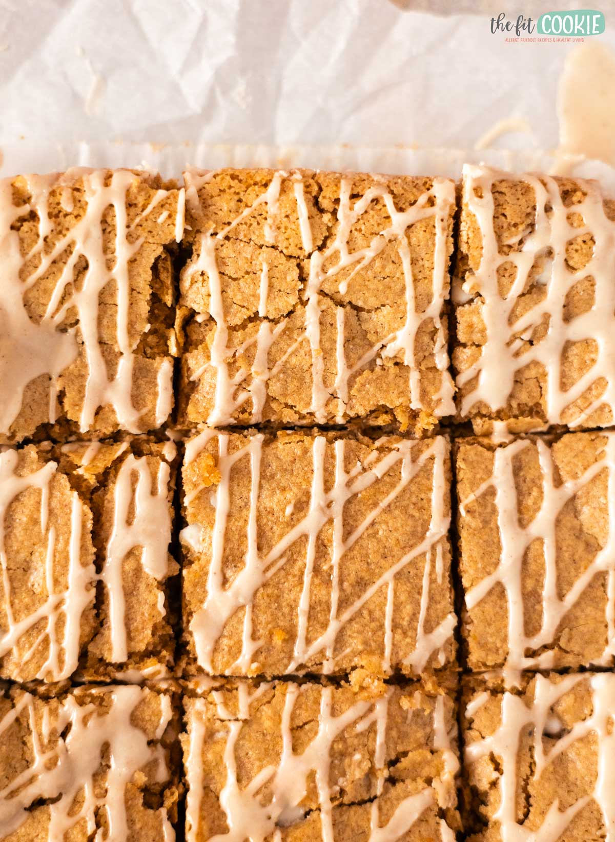 Overhead view of sliced cinnamon roll blondies with a white icing drizzle on parchment paper.