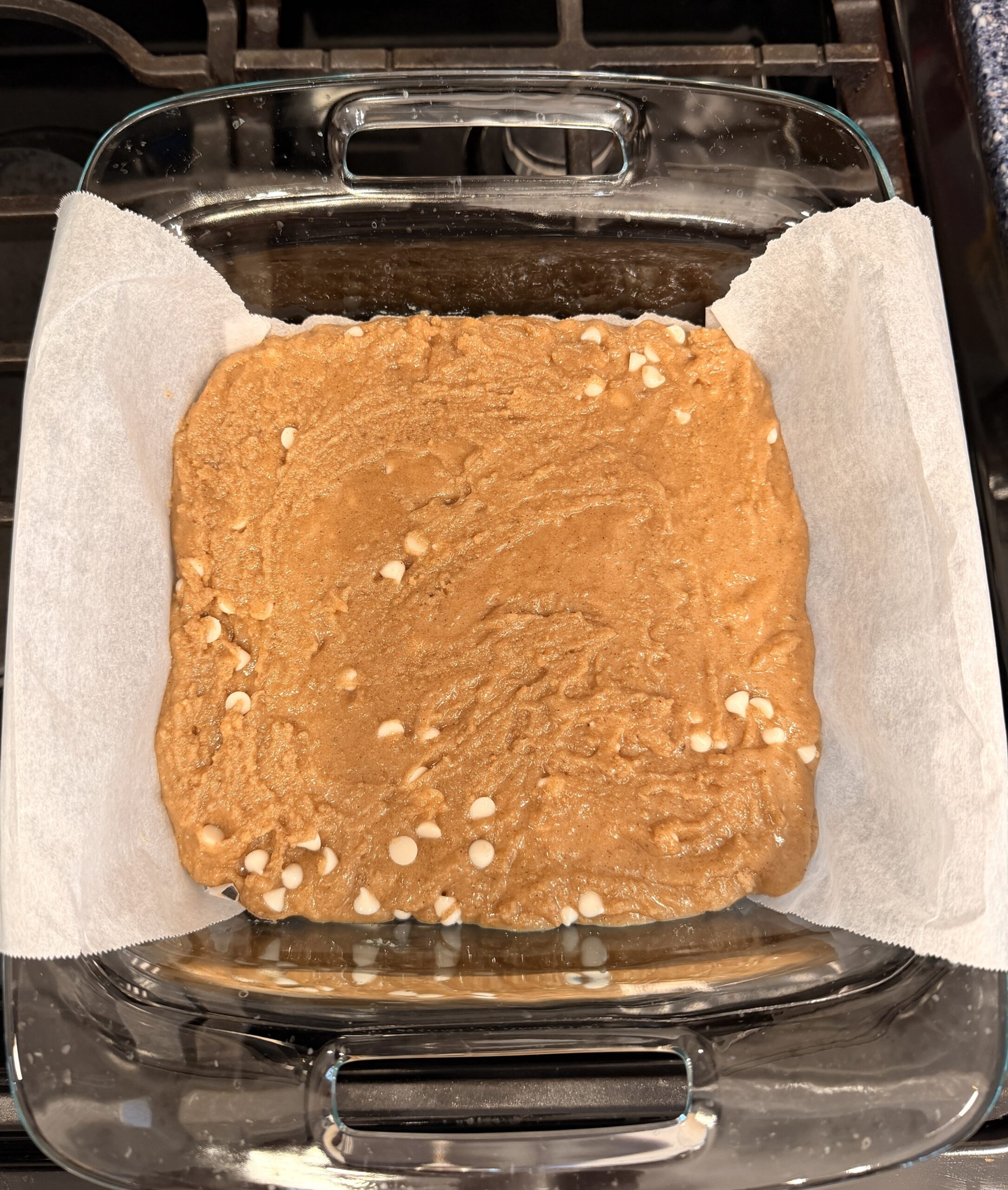 A glass baking dish lined with parchment paper holds unbaked cinnamon blondie batter.