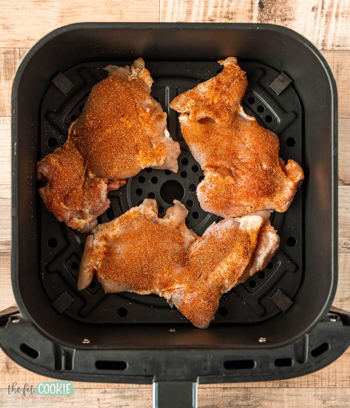 Three raw, seasoned chicken thighs arranged inside an air fryer basket.