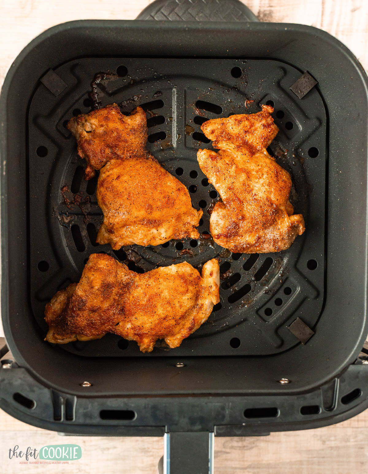 Seasoned and cooked chicken thighs inside an air fryer basket.