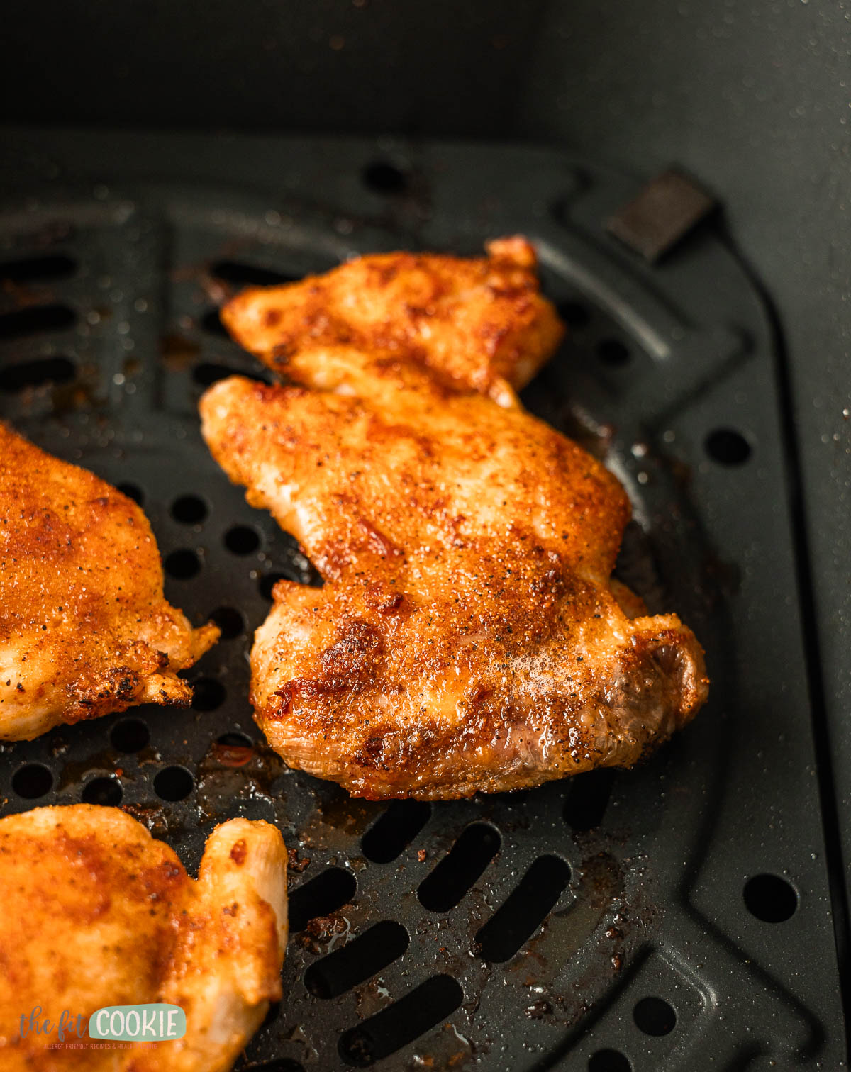 Close up photo of seasoned and air fried chicken thighs in an air fryer basket.