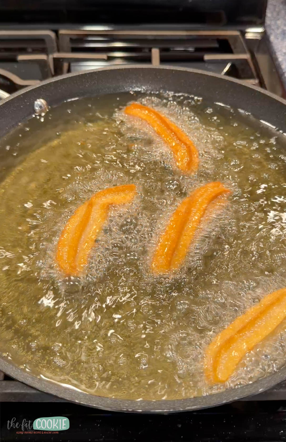 Four vegan churros frying in hot oil in a pan on a stove.