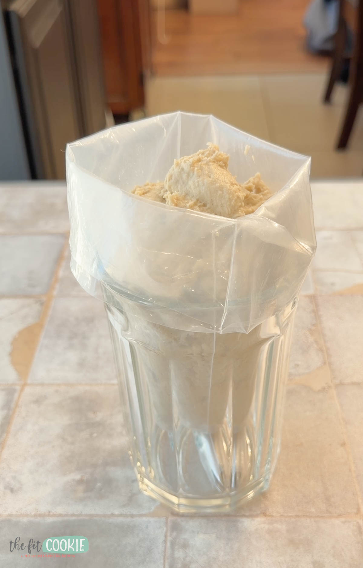A glass holds an open piping bag filled with thick vegan churro batter.
