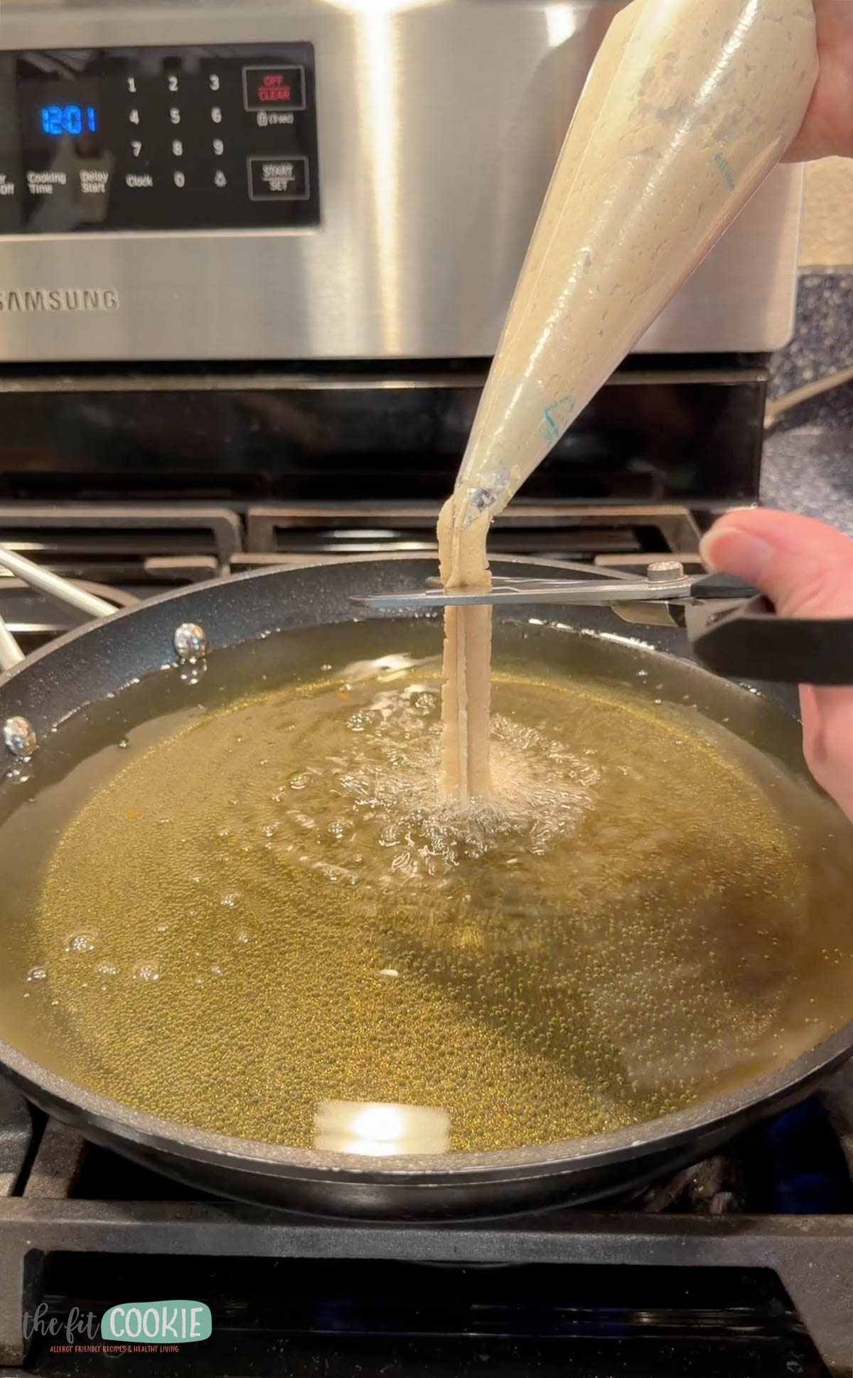 A person pipes batter for Gluten Free Vegan Churros from a pastry bag into hot oil on the stovetop.