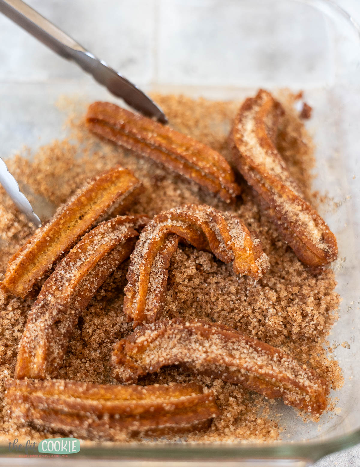 Several allergy friendly churros coated in cinnamon sugar are in a glass dish.